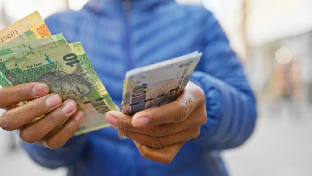 A woman holds south african rand on a city street.