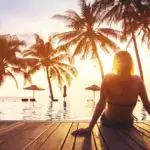 Woman relaxing on a pier in front of a pool and palm trees