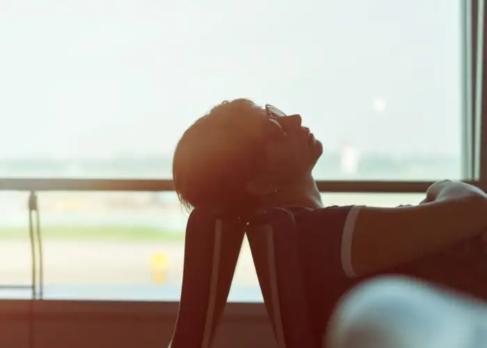 Woman backlit by airport window resting her head on a chair in an airport terminal