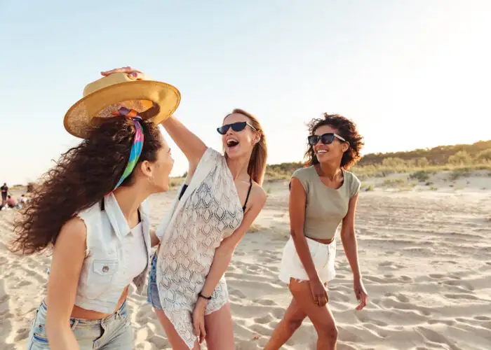 Three friends laughing and walking on the beach