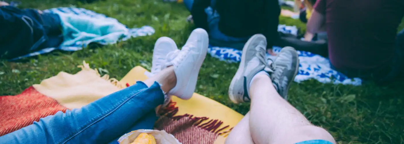 Two sets of legs resting on an outdoor blanket in a crowd