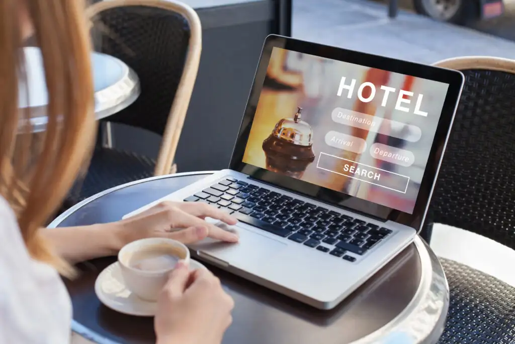 Over the shoulder view of a woman booking a hotel on a laptop in a cafe while drinking coffee