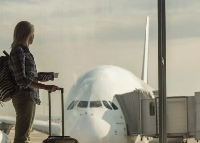 Woman with luggage standing in dark terminal in front of window