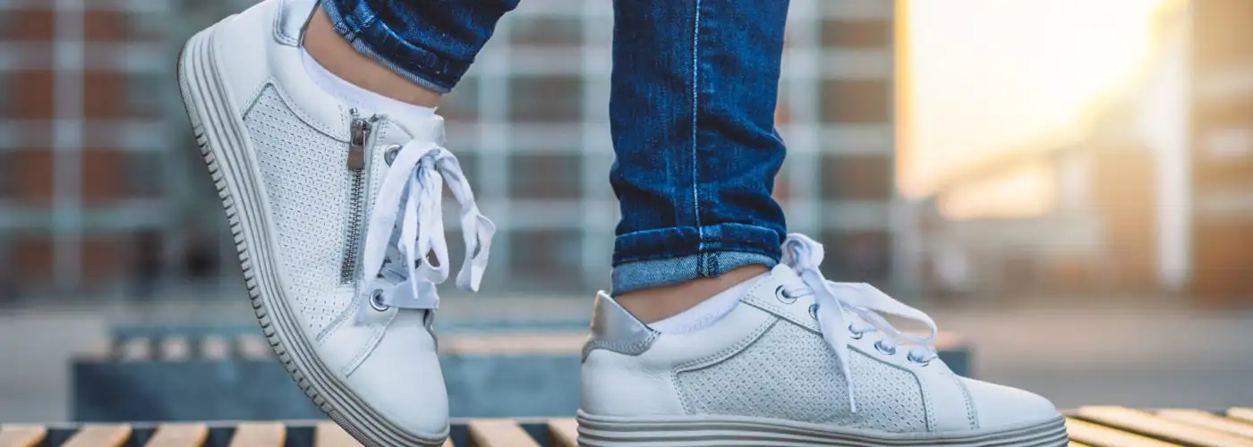 Woman wearing white sneakers walking in city at sunset