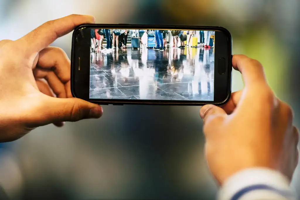 Close up of person's hands taking a photo of people's legs and luggage at the airport