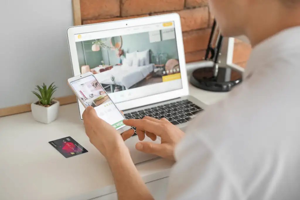 Person using a smartphone and laptop to book a hotel room