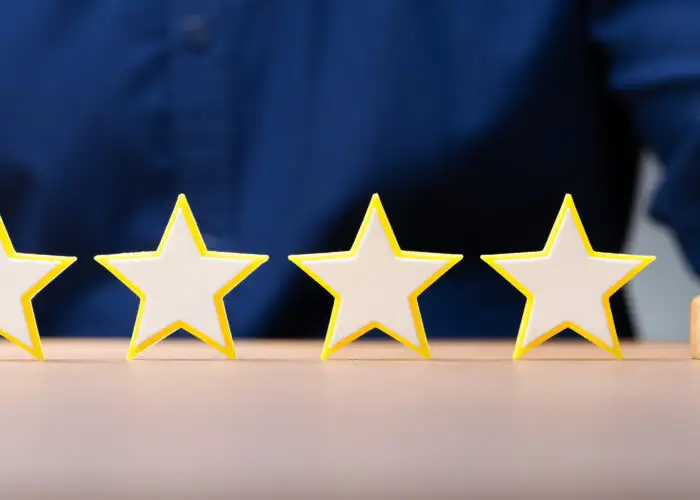 Five wooden stars lined up on a table next to a bell, which is being rung by a hotel worker in white gloves