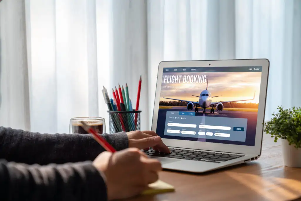 Close up of person typing on computer with one hand and writing in a notebook with the other hand while booking flights