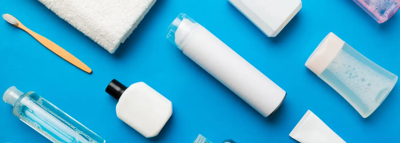 Overhead view of several travel toiletries laid out on a blue background