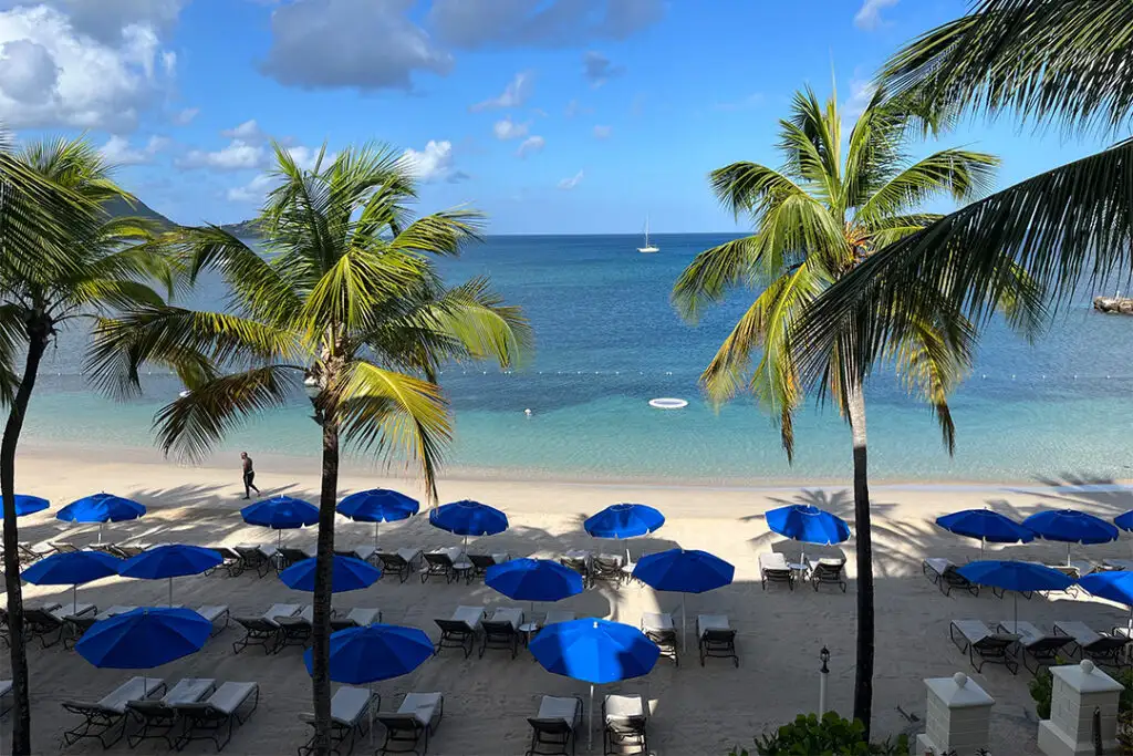 Lounge chairs on the beach surrounded by palm trees as seen from a suite deck at The Landings Resort and Spa in Saint Lucia