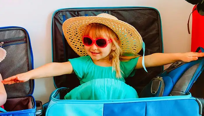 Children playing inside suitcases next to packed luggage