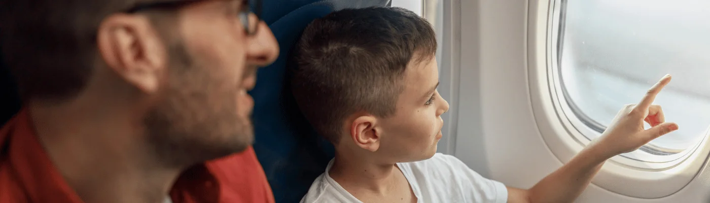 Curious little boy looking out the window while traveling by plane together with his father. Family, transportation, vacation concept