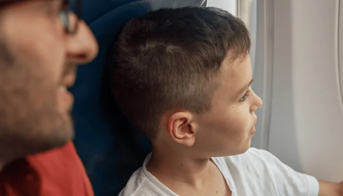 Curious little boy looking out the window while traveling by plane together with his father. Family, transportation, vacation concept