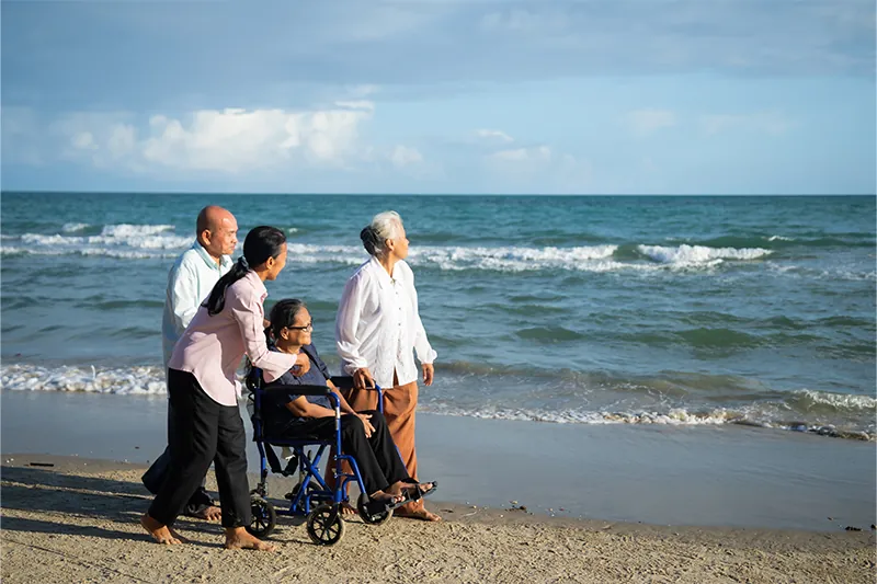 Elderly woman in beach wheelchair by the sea surrounded by friends