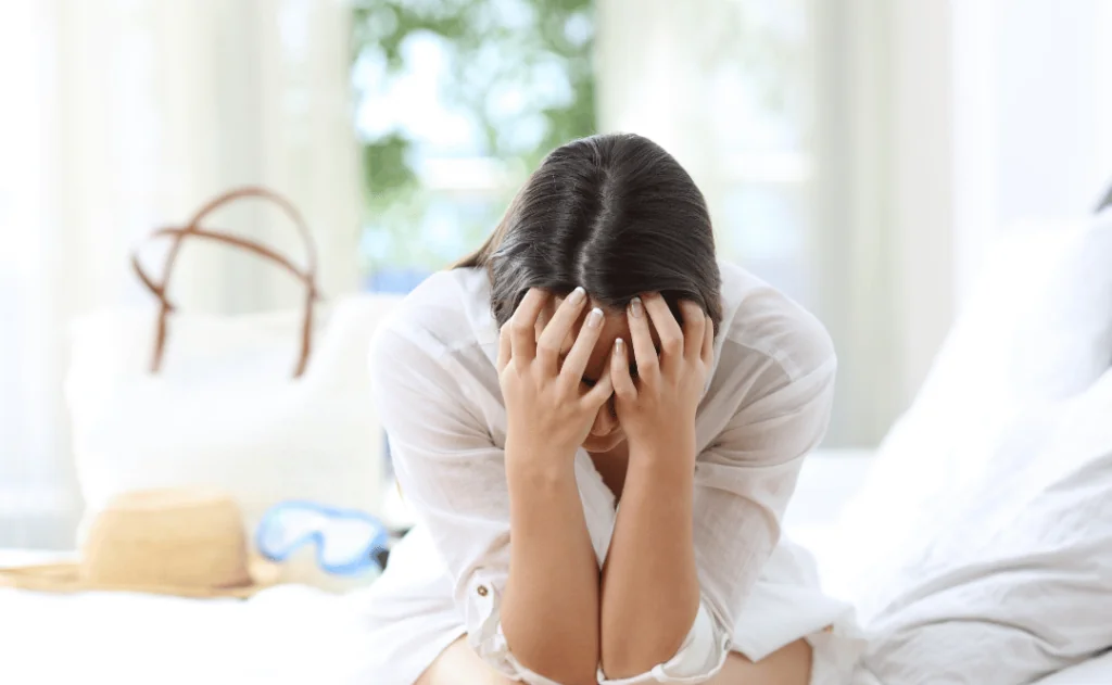 Frustrated woman sitting on bed in hotel room while on vacation 