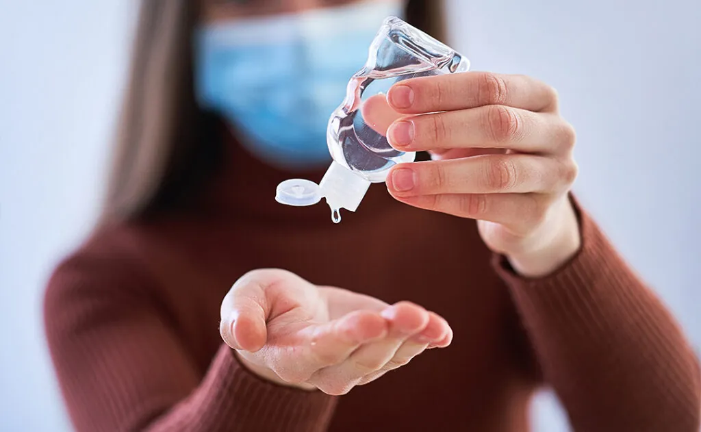 Woman in medical protective mask applying an antibacterial antiseptic gel for hands disinfection and health protection during during flu virus outbreak. Coronavirus quarantine and novel covid ncov