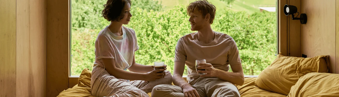 happy couple holding cups of morning coffee next to window with beautiful view, banner