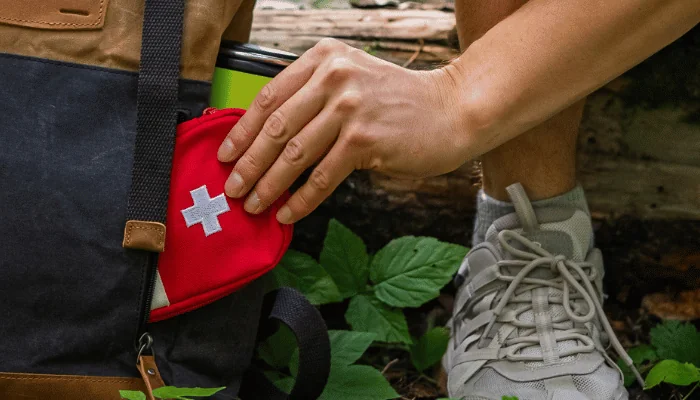 Hiker man crouching in a forest, packing a first aid kit into a backpack, emphasizing preparedness and safety during outdoor adventures