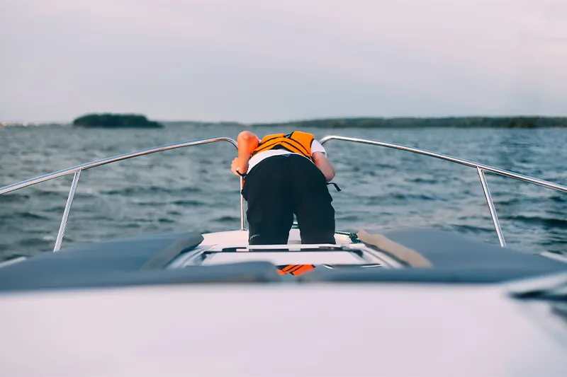 Man wearing life jacket leaning over the railing of a ship, motion sick