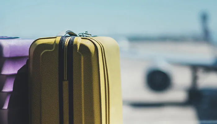 Suitcases sitting in front of large window at airport, through which an out-of-focus airplane can be seen