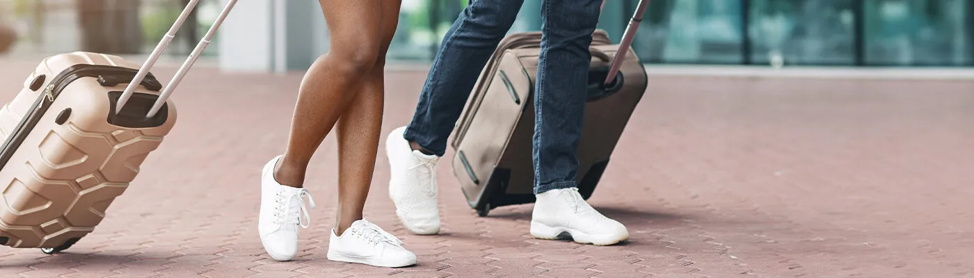 A couple walks through an airport terminal, each pulling a suitcase behind them.