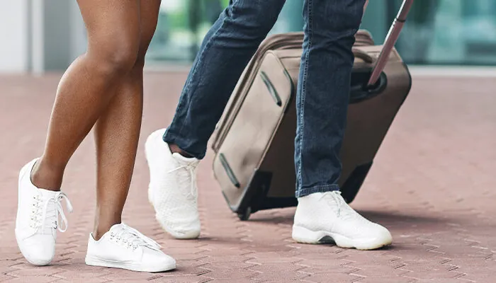 A couple walks through an airport terminal, each pulling a suitcase behind them.