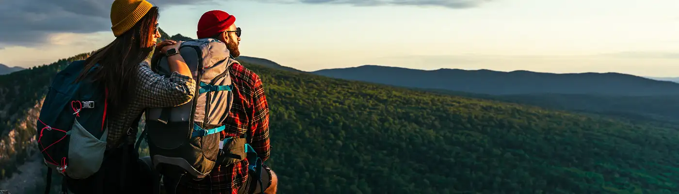 The couple meets the sunset in the mountains. Two travelers are sitting on the edge of a cliff and admiring the beautiful panoramic view. Travelers with backpacks at sunset in the mountains. Panorama