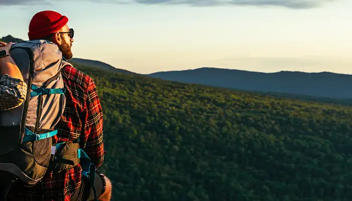 The couple meets the sunset in the mountains. Two travelers are sitting on the edge of a cliff and admiring the beautiful panoramic view. Travelers with backpacks at sunset in the mountains. Panorama