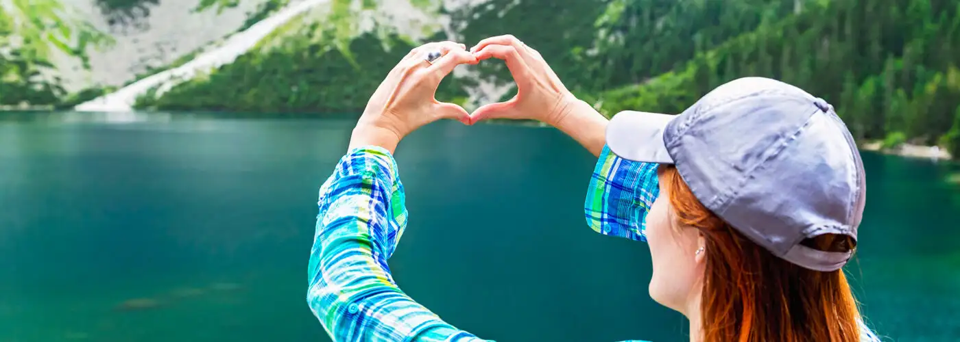 Girl make heart sign (shape of heart) on like, mountains background. In love with nature. Eye of the Sea lake (Morskie Oko). Tatra mountains. Poland.