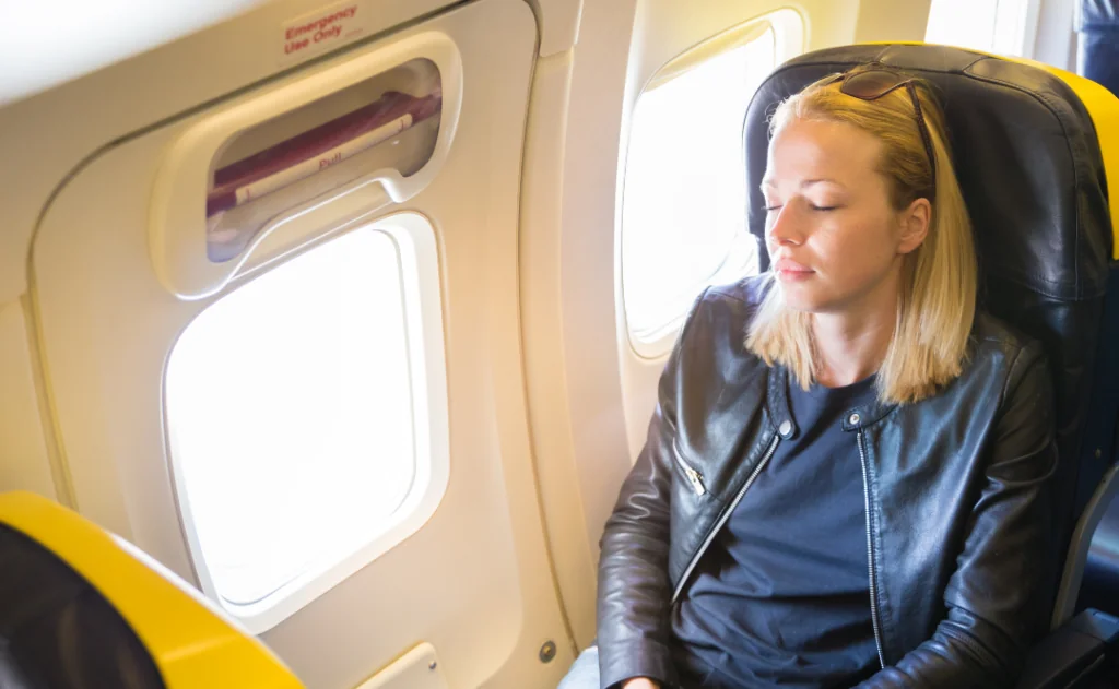 Women napping on exit window seat while traveling by airplane